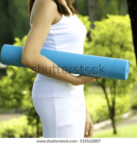 Lady is preparing for yoga in the park by holding blue mat and wear white sport dress