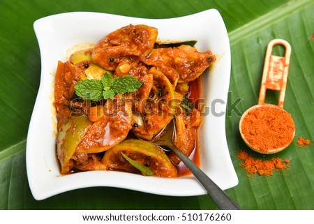 Indian lemon pickle, traditional homemade red hot and spicy, Kerala, South India. Tangy fresh lime picked in chilli, turmeric powder, with ginger and garlic. In a white dish/plate on green banana leaf
