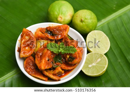Indian lemon pickle, traditional homemade red hot and spicy, Kerala, South India. Tangy fresh lime picked in chilli, turmeric powder, with ginger and garlic. In a white dish/plate on green banana leaf