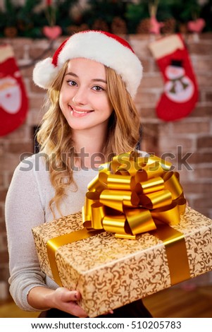 Beautiful young blonde girl in the hat of Santa Claus with a gift in the hands in the room with the Christmas decor.
