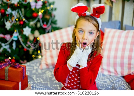 happy child girl with rabbit ears near a decorated Christmas tree surprized by Christmas gifts