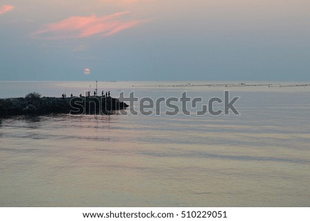 Peaceful summer morning at sunrise, calm sea, silhouettes of fishermen on breakwater, fish farm in the distance