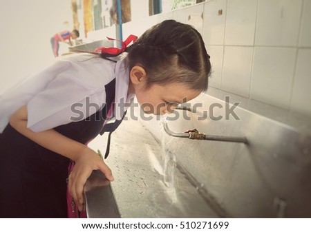 An asian girl in the uniform is drinking water from a tap at the school  after played hard in a hot and sunny day. Vintage tone , fade picture.