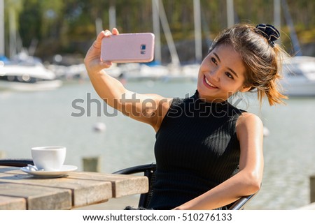 Beautiful Asian woman smiling and taking selfie picture with mobile phone outdoors