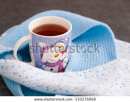  Tea in a mug with a picture of a snowman. Tea in winter and snowman. Image Snowman recalls the new year and the cold. Knitted scarf warm in the new year. Tea shrouded in a scarf. 