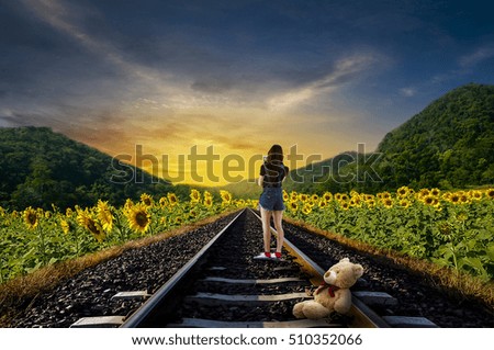 
A little girl with a teddy bear standing on the tracks at sunset Sunflower light beautifully.