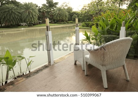 White chair and stool on brown corridor in the garden beside lake