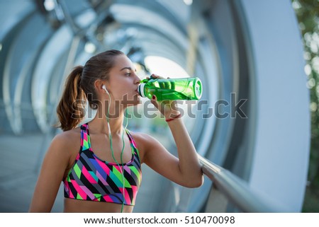Healthy young woman drinking water and listening to music after exercising. Hydrating is very important because it regulates body temperature, helps transport nutrients, and lubricates your joints.