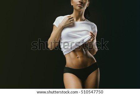 Close-up photo of strong woman with muscular abdomen in sportswear. Fitness female model posing on black background. Beautiful woman with clean and glowing skin isolated on dark background.