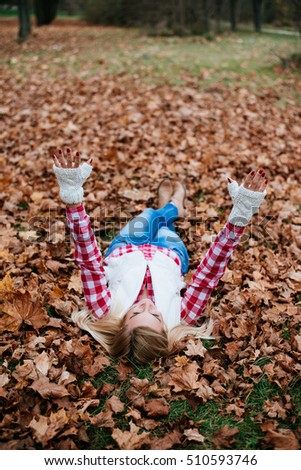 woman lying on autumn leaves, arms up in the sky