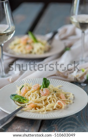 two servings of spaghetti with shrimp and spinach, a piece of cheese grater and two glasses of white wine
