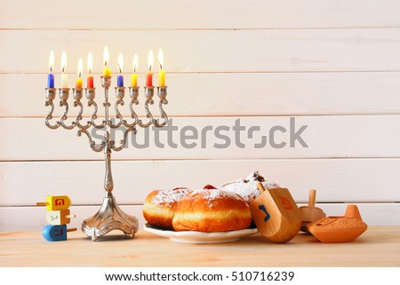 Image of jewish holiday Hanukkah with menorah (traditional Candelabra), donuts and wooden dreidel (spinning top)