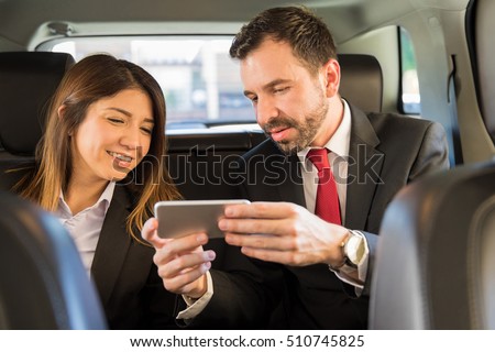 Portrait of two young businesspeople riding in the backseat of a car and looking at a smartphone