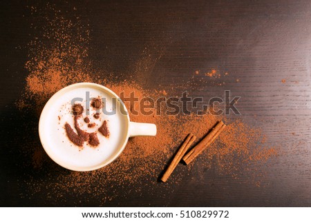 Cup of coffee with panda pattern of cinnamonon dark background