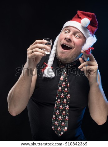 Comic actor man in cap with braids with a glass of vodka on a black background, in anticipation of Christmas and New Year
