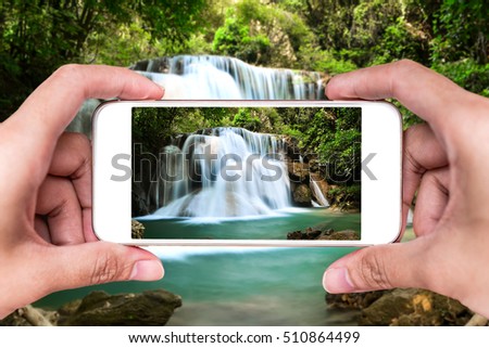 Making photos by smartphone of amazing waterfall in autumn forest 