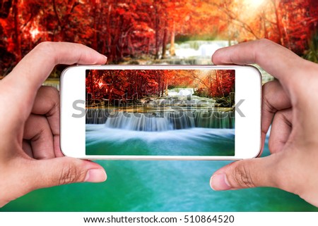 Making photos by smartphone of amazing waterfall in autumn forest 