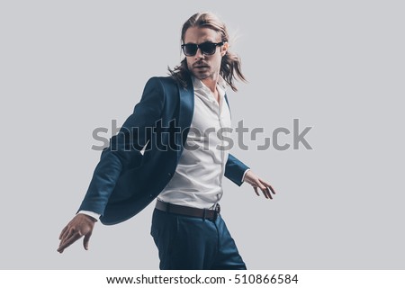 Style in motion. Handsome young man in full suit and sunglasses moving in front of grey background Royalty-Free Stock Photo #510866584
