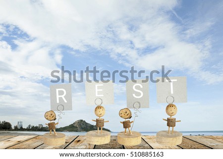 Wooden Blank Sign With Text  REST , Over Blurred blue sea and  beach with Cloudy Blue Sky .
