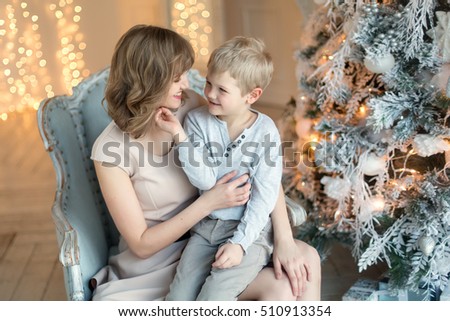 beautiful mother and son looking at each other, sitting in a chair at the  Christmas tree decorated with snow. New Year Christmas