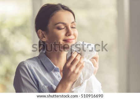 Beautiful young woman is smelling clean clothes and smiling while doing laundry at home Royalty-Free Stock Photo #510916690