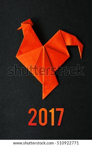 Red fire paper folded rooster handmade origami craft on black background. Nice natural holiday greeting card. 2017 lettering.