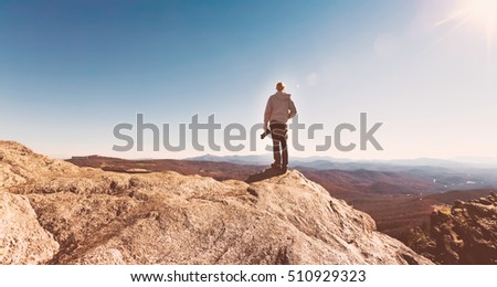 Man with a camera on top of a cliff overlooking the mountains