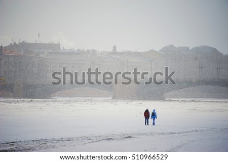 Two young people crossing on the ice of the river Neva in winter during snowfall in Central St. Petersburg.