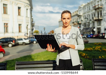 the girl has decided to come for walk. On the street a good and sunny weather. the girl performs work behind the laptop. The sun pinches her eyes.