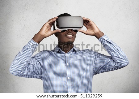 Technology, innovation and cyberspace concept. Amazed African employee in blue shirt having fun and entertaining himself while playing video games in office during break, using oculus rift headset