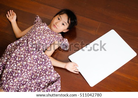 Little Asian child laying down on the wooden background with a blank white board