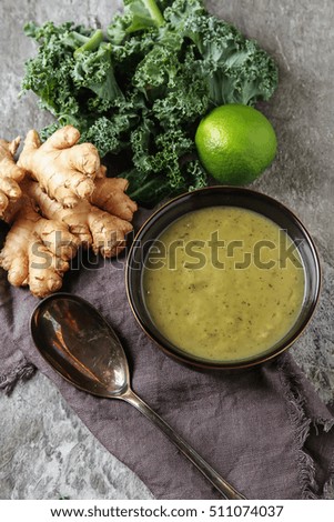 Classic pea soup puree in a black plate with a spoon, lime, ginger and cabbage Kale. Grey stone background.