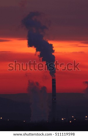 Smoking chimney of coal factory in industrial area during sunset with orange and red background
