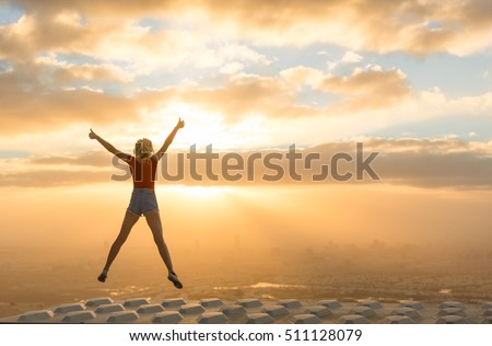 Success concept. Celebrating woman on top of skyscraper overlooking the city at sunrise.  Royalty-Free Stock Photo #511128079