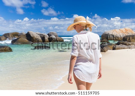 Woman wearing white loose tunic over bikini and beach hat on Mahe Island, Seychelles. Summer vacations on picture perfect tropical beach concept.