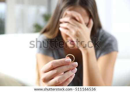 Closeup of a single sad wife after divorce lamenting holding the wedding ring in a house interior Royalty-Free Stock Photo #511166536