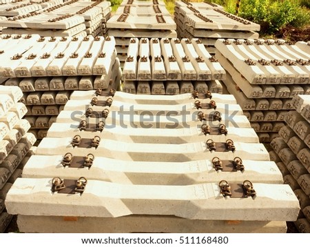 Sleepers stock in railway depot. Concrete railway ties stored for reconstruction of old railway station. Old houses and highway bridge in background