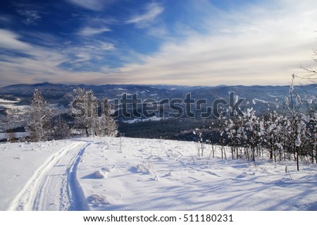 Winter snow mountain hills and the track path of the snowmobile in the foreground under blue sky. Altai Mountains, Siberia, Russia