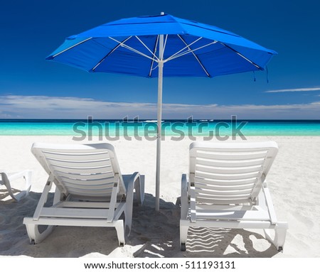 Caribbean beach with blue sun umbrellas and white beds. Tropical vacation
 Royalty-Free Stock Photo #511193131