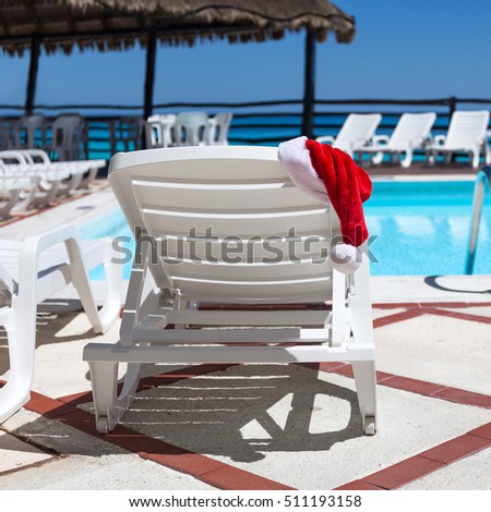 Santa Claus Hat on sunbed near swimming pool. Christmas vacation concept Royalty-Free Stock Photo #511193158