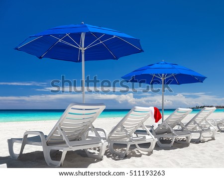 Caribbean beach with blue sun umbrellas and white sunbeds. Christmas vacation. Santa hat on sun chair
 Royalty-Free Stock Photo #511193263
