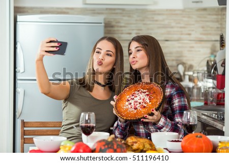 Two young women are taking selfies with their smart phone. They are taking pictures of food they made for Thanksgiving dinner.