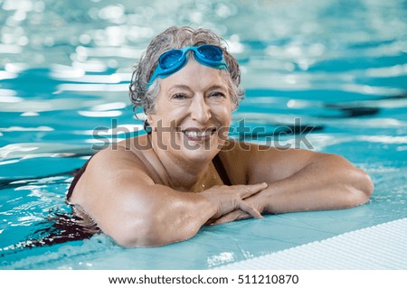 Mature woman wearing swim goggles at swimming pool. Fit active senior woman enjoying retirement  in swimming pool and looking at camera. Happy senior healthy old woman enjoying active lifestyle. Royalty-Free Stock Photo #511210870