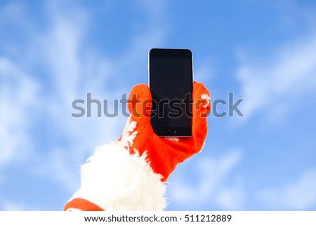 Santa claus with mobile phone ready for Christmas time on sunny blue sky outdoors background