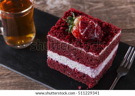 A slice of red velvet cake with white frosting is garnished with strawberries  close up