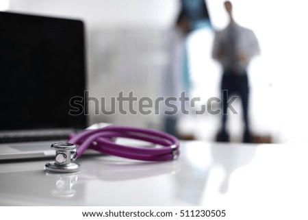 Laptop and medical stethoscope on the desk , doctors standing in the background.