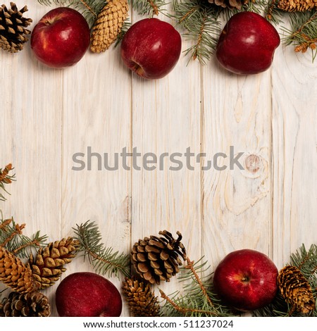 Christmas apples and spruce branches with cones on white wooden Board.