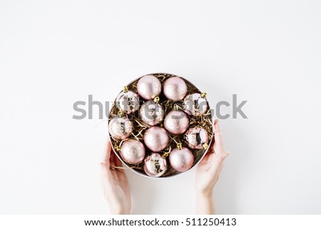 female hands holding round box with bright christmas balls on white background. flat lay, top view