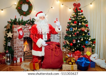 Santa Claus at the Christmas tree with a gift in her hand smiling at Christmas, New Year in room with decor.