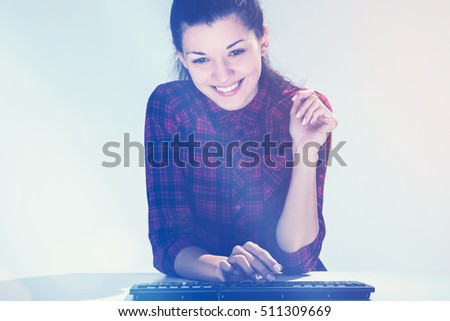 Smiling woman in red shirt is sitting at her keyboard and communicating in a chat. Concept of social media. Mock up. Toned image